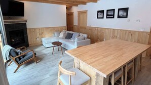 Una habitación acogedora con techo de madera, chimenea, sofá, mesa de comedor y televisor.