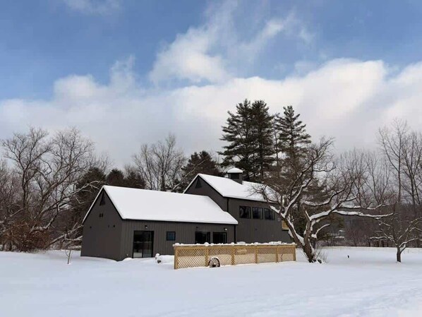 A two-story building with a snow-covered roof, surrounded by bare trees and a clear sky.