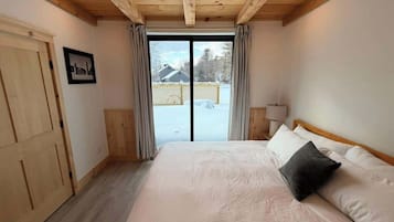 Un dormitorio con una cama grande, techo de madera, puerta corrediza de vidrio y vista a un paisaje nevado.