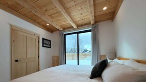 Un dormitorio con una cama grande, vigas de madera en el techo, un ventanal corredero a un balcón y un cuadro en la pared.