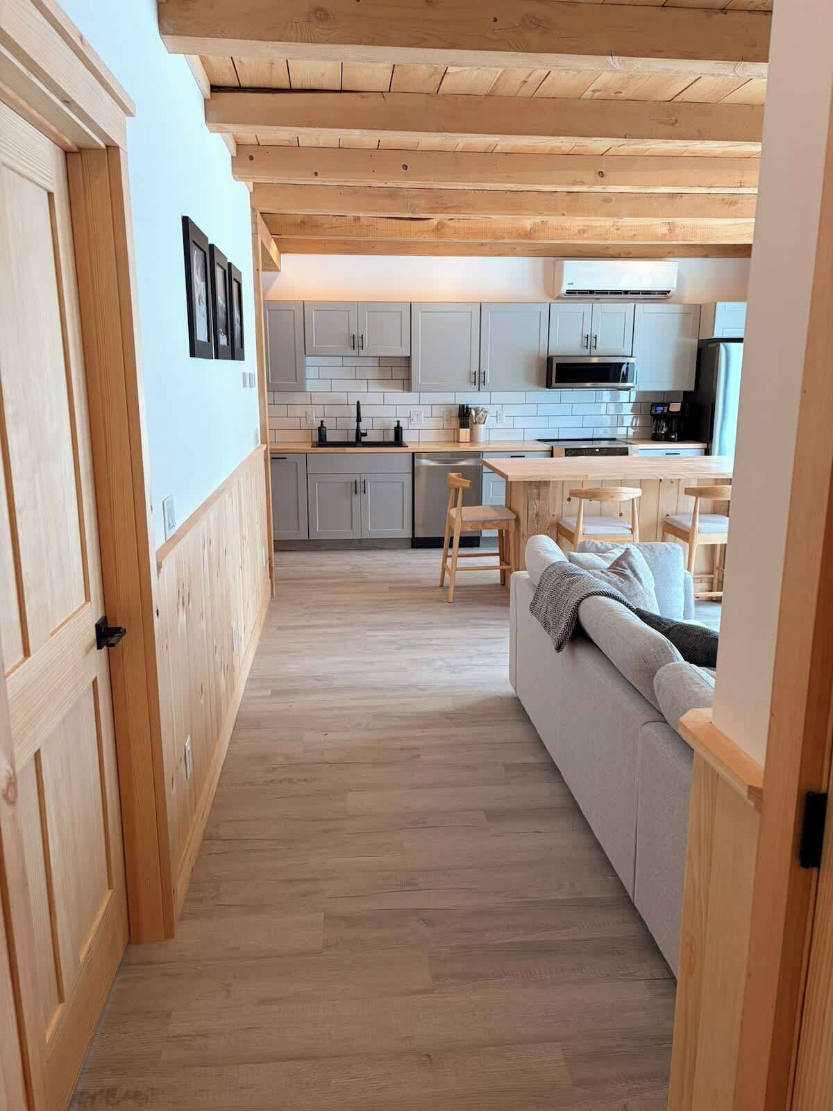 Una cocina moderna con armarios blancos, techo de madera y un comedor con sofá y sillas.