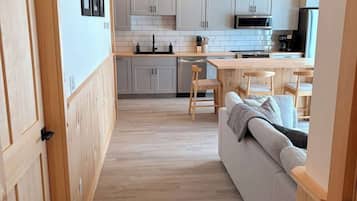 Una cocina moderna con armarios blancos, techo de madera y un comedor con sofá y sillas.