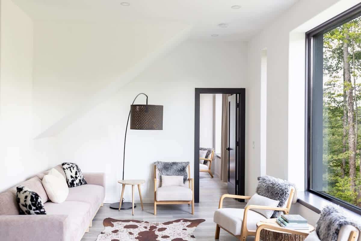 A modern living room with a sofa, chairs, a floor lamp, and a view through a large window.