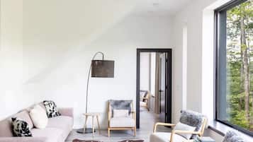 A modern living room with a sofa, chairs, a floor lamp, and a view through a large window.