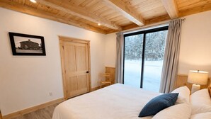 Ein Schlafzimmer mit einem großen Bett, Holzbalkendecke, einem Fenster mit Vorhängen und einem gerahmten Bild an der Wand.