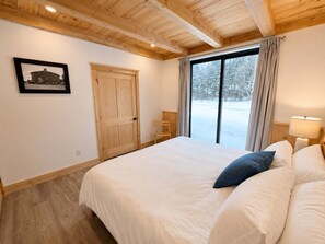 A bedroom with a large bed, wooden ceiling beams, a window with curtains, and a framed picture on the wall. - Bear Hearth | Nordic Barn, Stowe Nature Escape (Stowe)