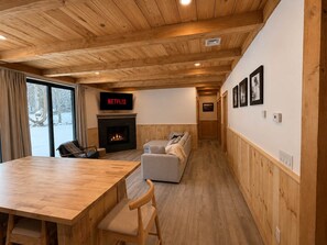 A cozy room with a fireplace, a sofa, a dining table, and a TV displaying 'NETFLIX'. - Bear Hearth | Nordic Barn, Stowe Nature Escape (Stowe)