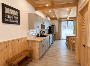 A modern kitchen with wooden cabinets, a built-in oven, and a dining area with a bench. - Bear Hearth | Nordic Barn, Stowe Nature Escape (Stowe)