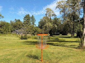 A grassy field with a disc golf basket and a house in the background. - Bear Hearth | Nordic Barn, Stowe Nature Escape (Stowe)