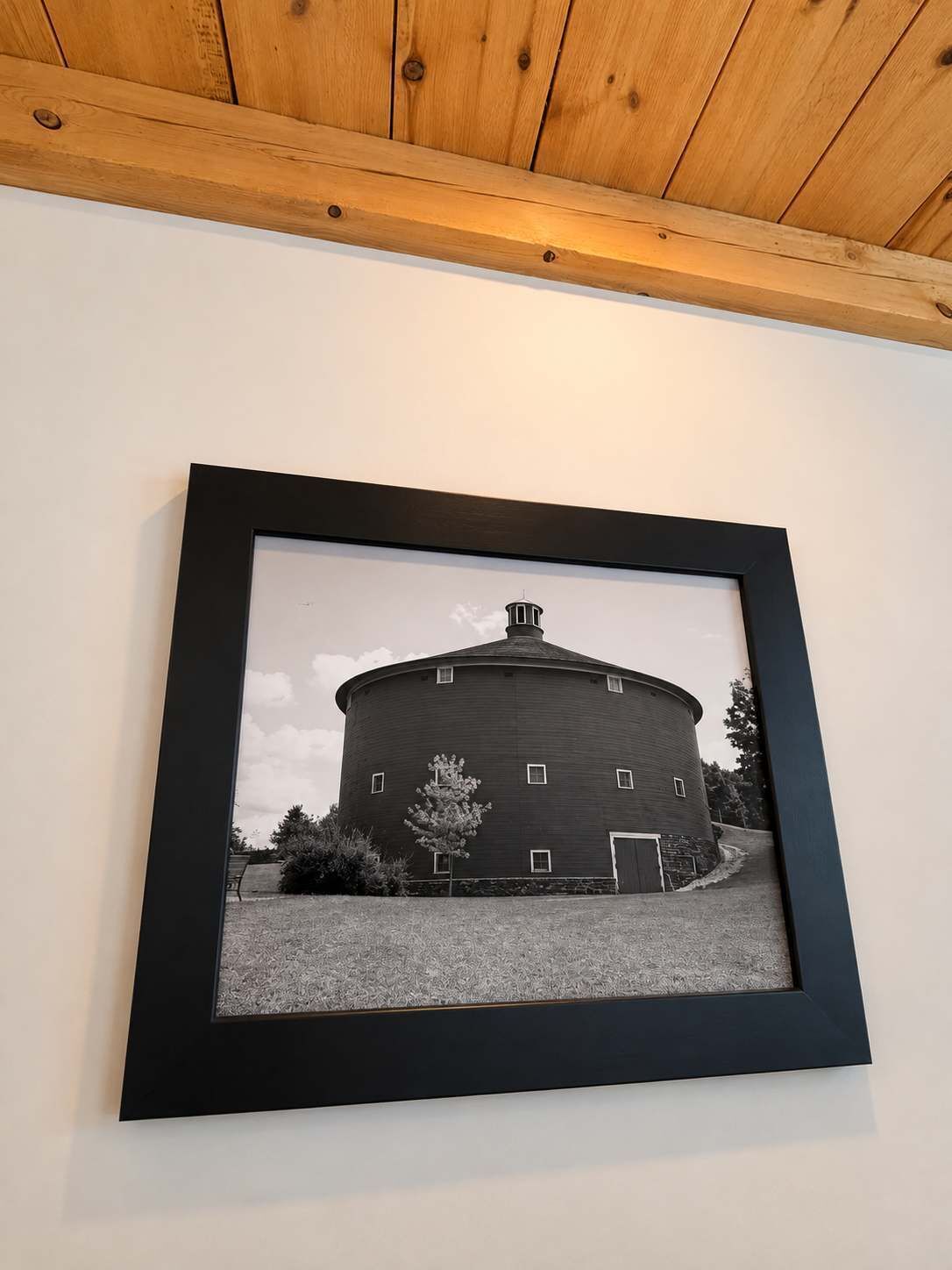 A framed black and white photograph of a round building with a central tower, possibly a silo, mounted on a wall.