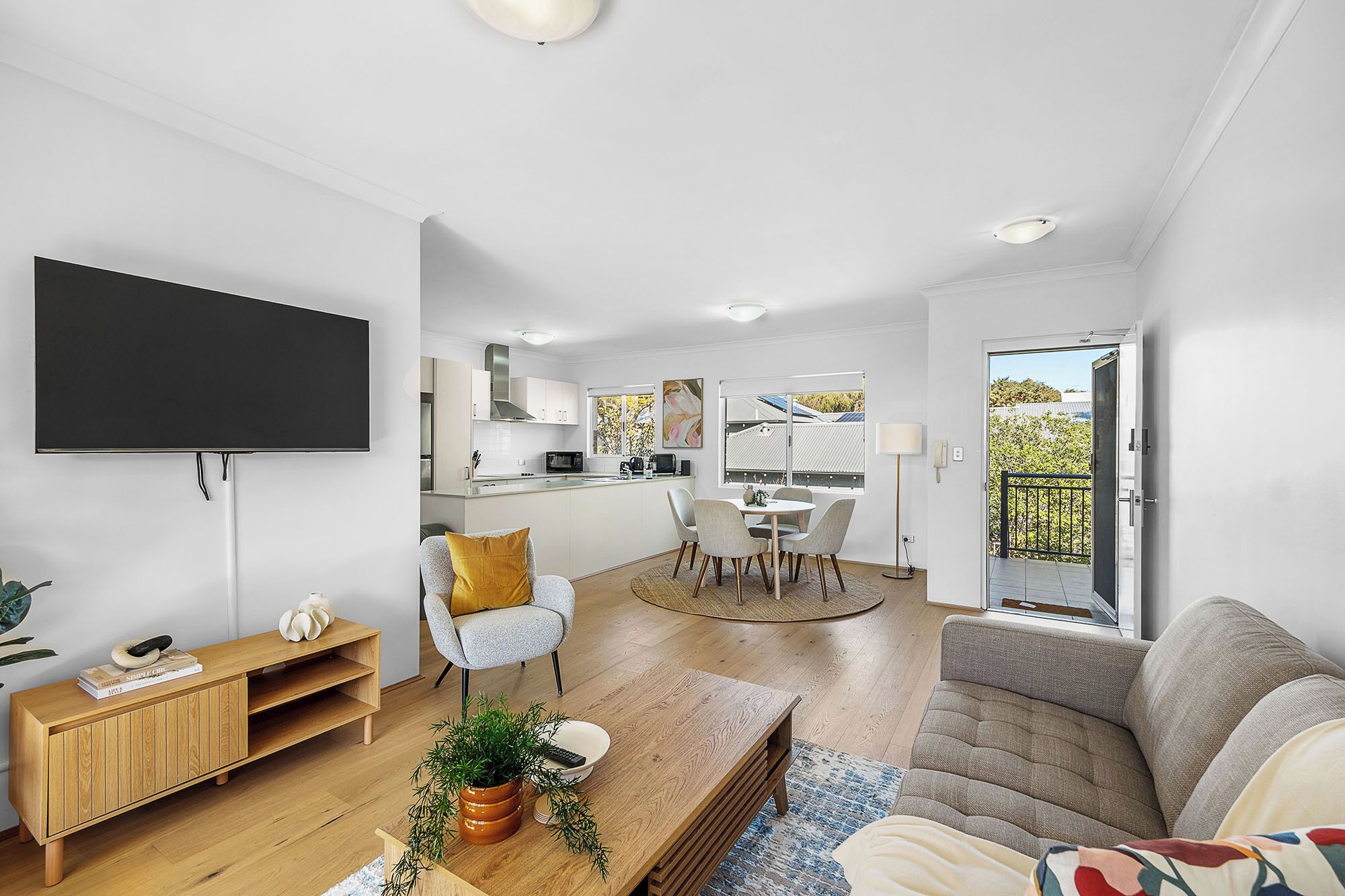 A modern living room with a flat-screen TV, a wooden TV stand, a sofa, and a dining area with a table and chairs.