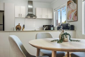 Eine moderne Küche mit weißen Schränken, einer Edelstahl-Dunstabzugshaube, einer Mikrowelle, einem Toaster und einem Esstisch mit Stühlen.