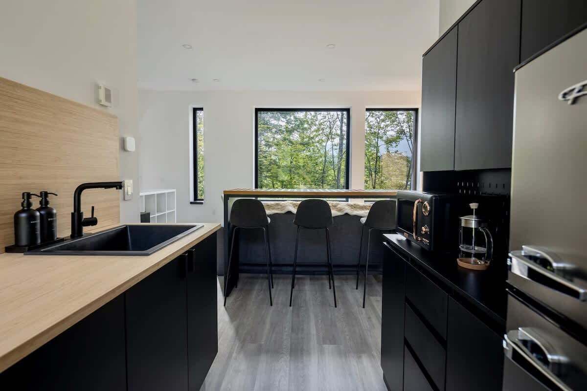 A modern kitchen with a central island, black cabinets, and a view through large windows.
