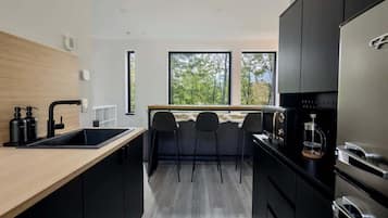 A modern kitchen with a central island, black cabinets, and a view through large windows.