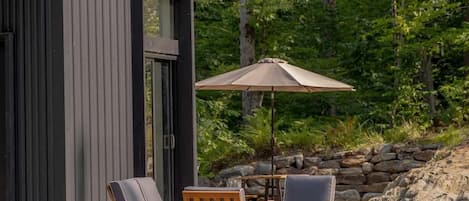 A modern building with a large sliding door, two lounge chairs, and a single umbrella.
