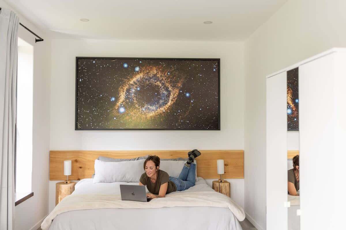 Une chambre d’hôtel avec une grande œuvre d’art sur le thème de la galaxie au mur, un lit avec un ordinateur portable et une tête de lit en bois.