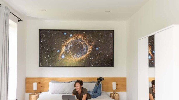 Ein Hotelzimmer mit einem großen Wandbild zum Thema Galaxie, einem Bett mit einem Laptop und einem hölzernen Kopfteil.