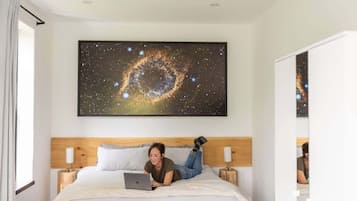 Habitación de hotel con una gran obra de arte temática de galaxia en la pared, una cama con una computadora portátil y un cabecero de madera.
