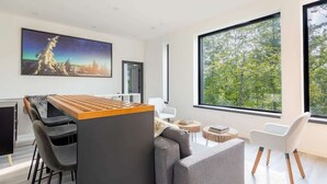 Ein modernes Interieur mit Essbereich, einer Couch und großen Fenstern mit Blick auf Bäume.