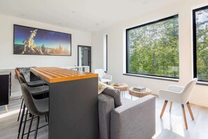 Um interior moderno com área de jantar, um sofá e grandes janelas com vista para árvores.