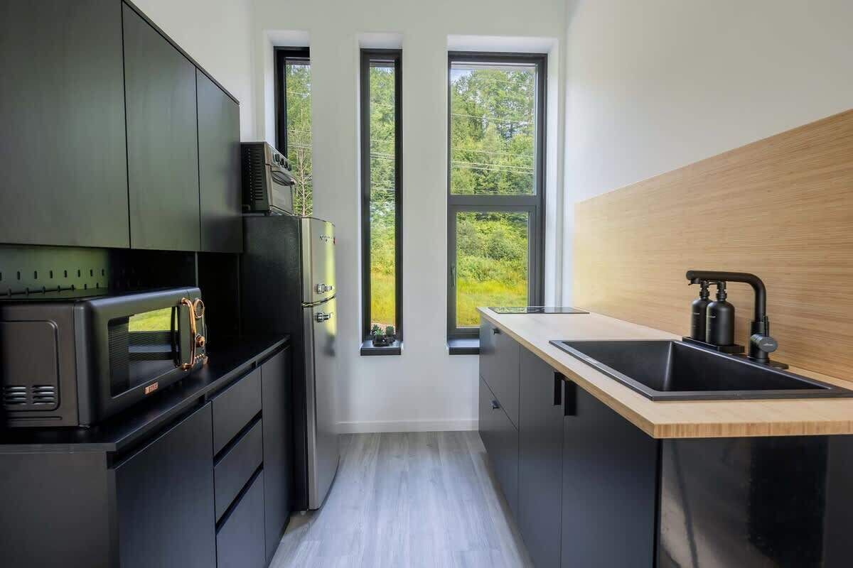 Une cuisine moderne dotée d’appareils électroménagers intégrés, d’un plan de travail en bois et offrant une vue à travers trois fenêtres.