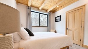 Un dormitorio con una cama de madera, una mesita de noche, una ventana con cortinas y un armario de madera.