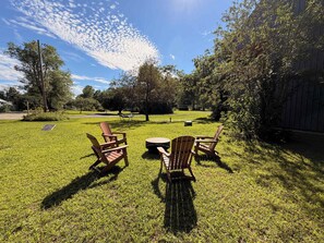 A grassy outdoor area with Adirondack chairs and a round table, surrounded by trees and a wooden fence. - Fox Perch | Nordic Design, Nature Escape in Stowe (Stowe)