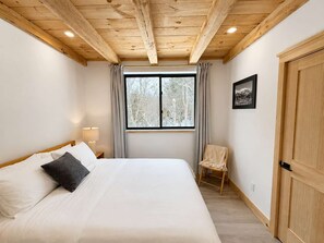 A bedroom with a wooden ceiling, a large window with curtains, a bed with white bedding, a chair, and a door. - Fox Perch | Nordic Design, Nature Escape in Stowe (Stowe)