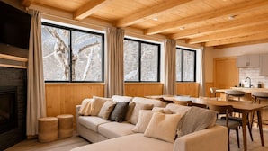 Una sala acogedora con un amplio sofá seccional color beige, una chimenea y un comedor con mesas y sillas de madera.