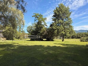 A grassy area with a volleyball net, surrounded by trees and a clear sky. - Fox Perch | Nordic Design, Nature Escape in Stowe (Stowe)