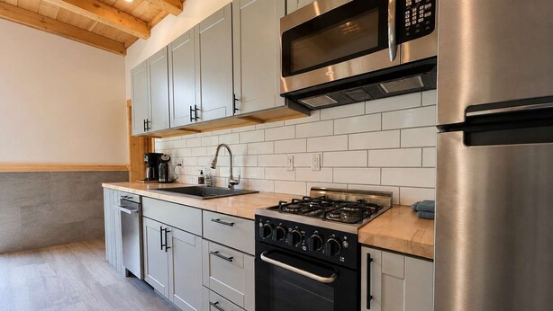 Una cocina moderna con electrodomésticos de acero inoxidable, armarios grises y encimera de madera.