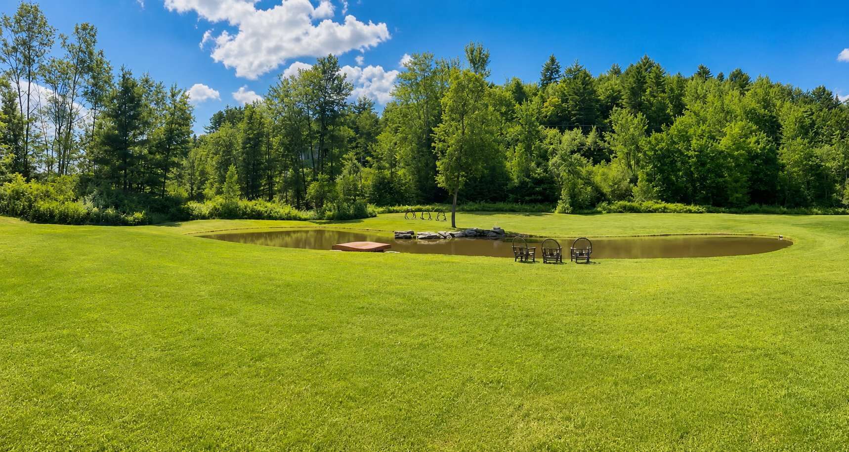 Golfkenttä, jossa on lampi, puita ja kirkas taivas.