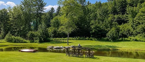A serene outdoor setting with a pond, a grassy area, and a seating arrangement.
