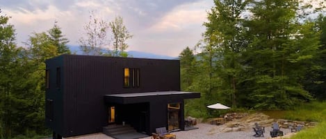 Un bâtiment moderne de couleur noire, doté d’un espace extérieur aménagé avec des sièges et d’une allée gravillonnée.