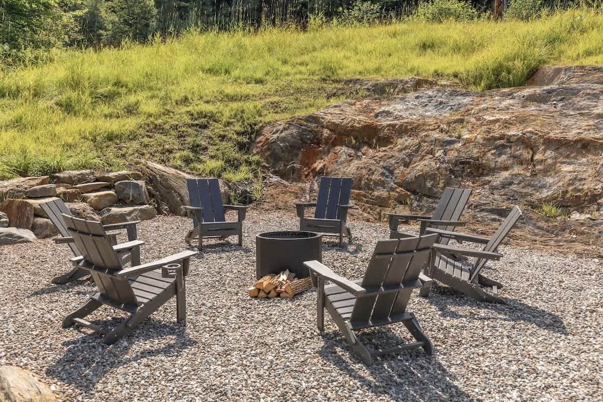A fire pit area with Adirondack chairs and a stone fire pit surrounded by gravel.