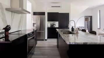 A modern kitchen with a central island, stainless steel appliances, and a marble countertop.