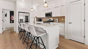 A modern kitchen with white cabinetry, a central island with bar stools, and pendant lighting. - Music-Themed Nashville Home | 4BR, 4 Baths & Bunk (Nashville)