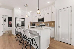 A modern kitchen with white cabinetry, a central island with bar stools, and pendant lighting. - Music-Themed Nashville Home | 4BR, 4 Baths & Bunk (Nashville)