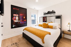 Ein modernes Schlafzimmer mit einem großen Bett, Stadtbild-Wandkunst, einem gerahmten Stadtbild und einem Spiegel mit Skyline.