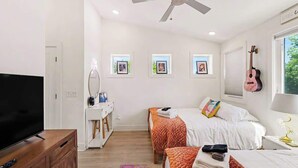 A bedroom with a TV, ceiling fan, two beds, a dresser, and framed pictures on the wall. - Music-Themed Nashville Home | 4BR, 4 Baths & Bunk (Nashville)