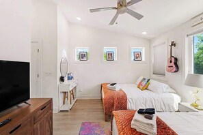 A bedroom with a TV, ceiling fan, two beds, a dresser, and framed pictures on the wall. - Music-Themed Nashville Home | 4BR, 4 Baths & Bunk (Nashville)
