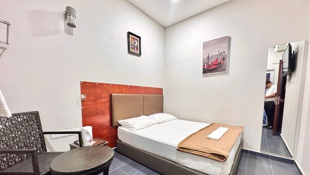 Una habitación de hotel pequeña con una cama individual, una mesita, una silla y un espejo.