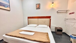 A neatly made bed with a brown blanket, a headboard, a small bedside table, a nightstand, a wall-mounted towel rack, and a picture of a rose. - The Ardens Hotel - Taman Desa Cemerlang (Johor Bahru)