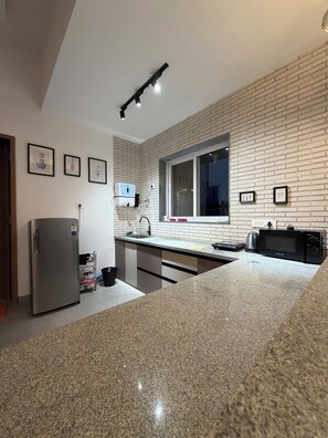 A modern kitchen with a granite countertop, stainless steel appliances, and a brick wall backsplash.