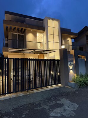 A modern two-story building with a gated entrance, a balcony, and a sign indicating it's a villa.
