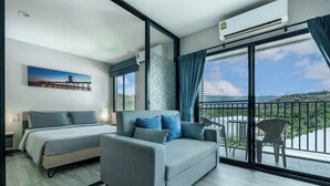 Habitación de hotel con cama, sofá, balcón con una silla y un cuadro en la pared.