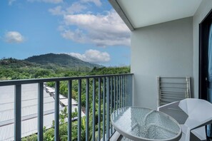 Un balcón con una mesa y sillas de vidrio, con vistas a una montaña y un edificio con techo de metal.