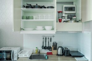 Una cocina con armarios blancos, microondas, tostadora y tetera.