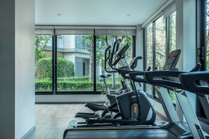 Une salle de sport équipée de matériel d’exercice et dotée de grandes fenêtres donnant sur un paysage verdoyant et des bâtiments.