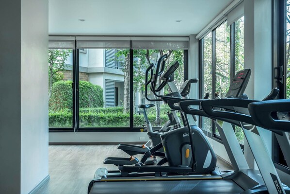 Ein Fitnessraum mit Trainingsgeräten und großen Fenstern, die Blick auf Grünflächen und Gebäude gewähren.